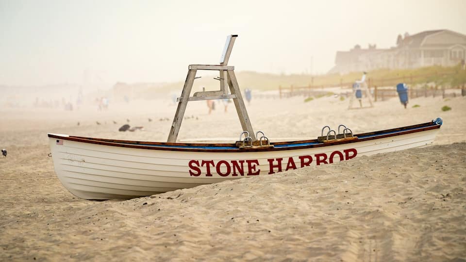 A boat named "STONE HARROP" on a sandy beach with a blurred background of people and a building.