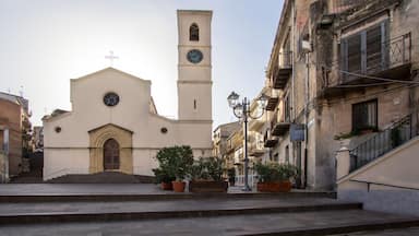 A church with a clock tower, steps leading to the entrance, and potted plants along the street.