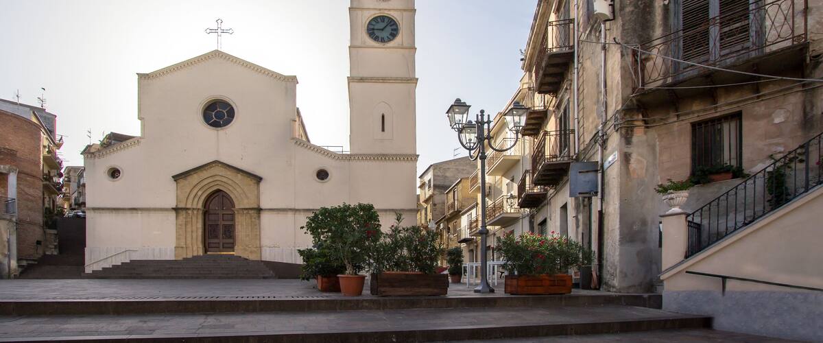 A church with a clock tower, steps leading to the entrance, and potted plants along the street.