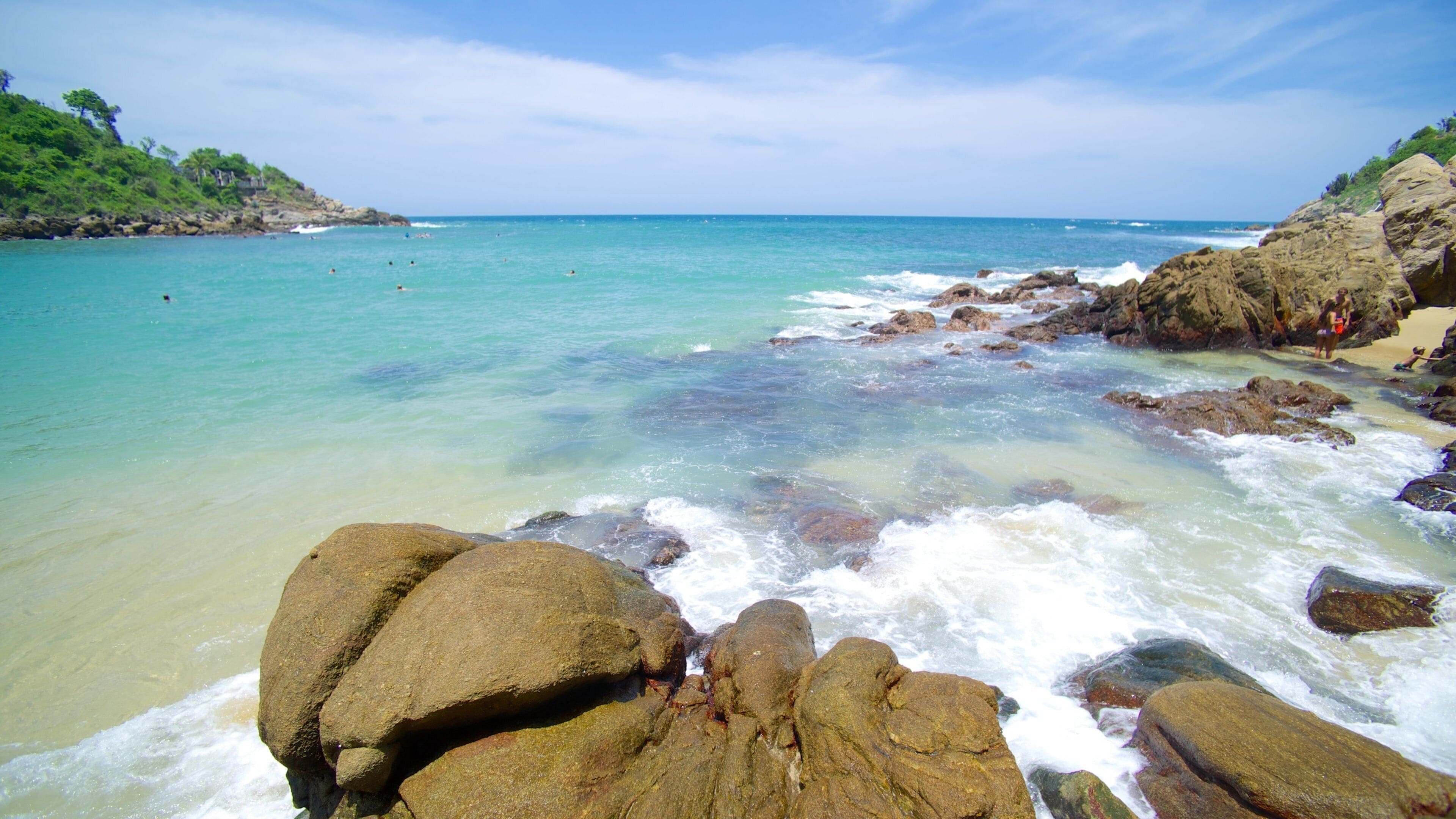 Una costa rocosa con agua turquesa cristalina y una playa a lo lejos.