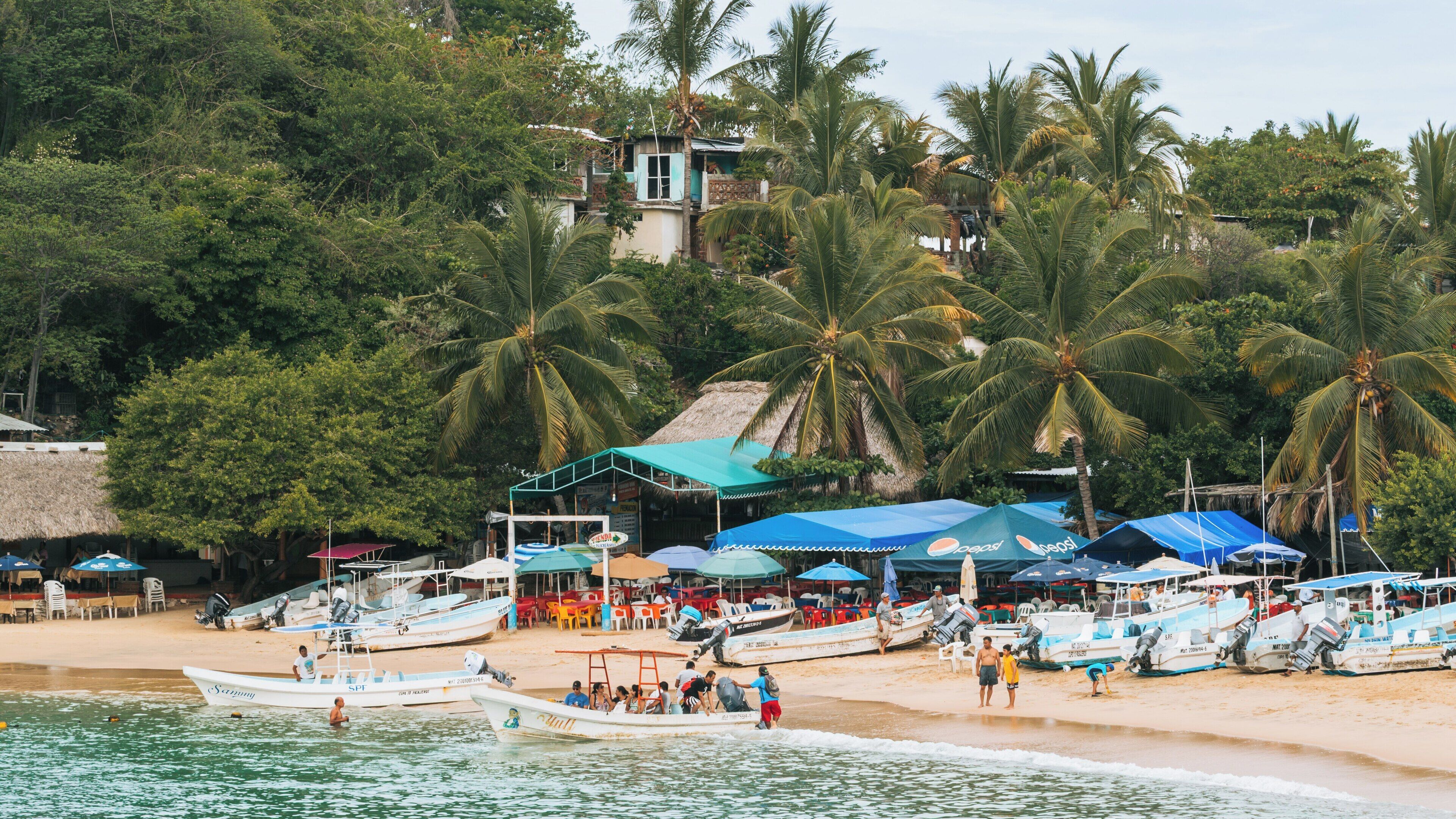 Puerto Angelito Beach in Puerto Escondido, Mexico offers scenic beauty and relaxation with local activities among palm trees and fishing boats