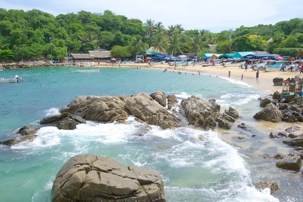 A beach with clear turquoise water, rocky shoreline, and lush green hills in the background.
