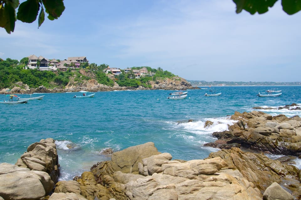 Un paysage côtier avec des rivages rocheux, une eau d’un bleu limpide et plusieurs petits bateaux.