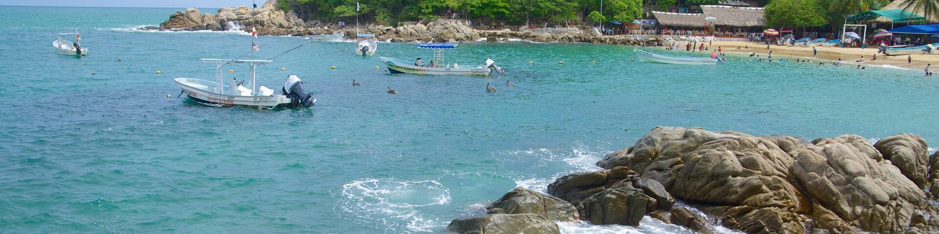A coastal scene with rocky shores, clear turquoise water, and a lush green hill in the background.