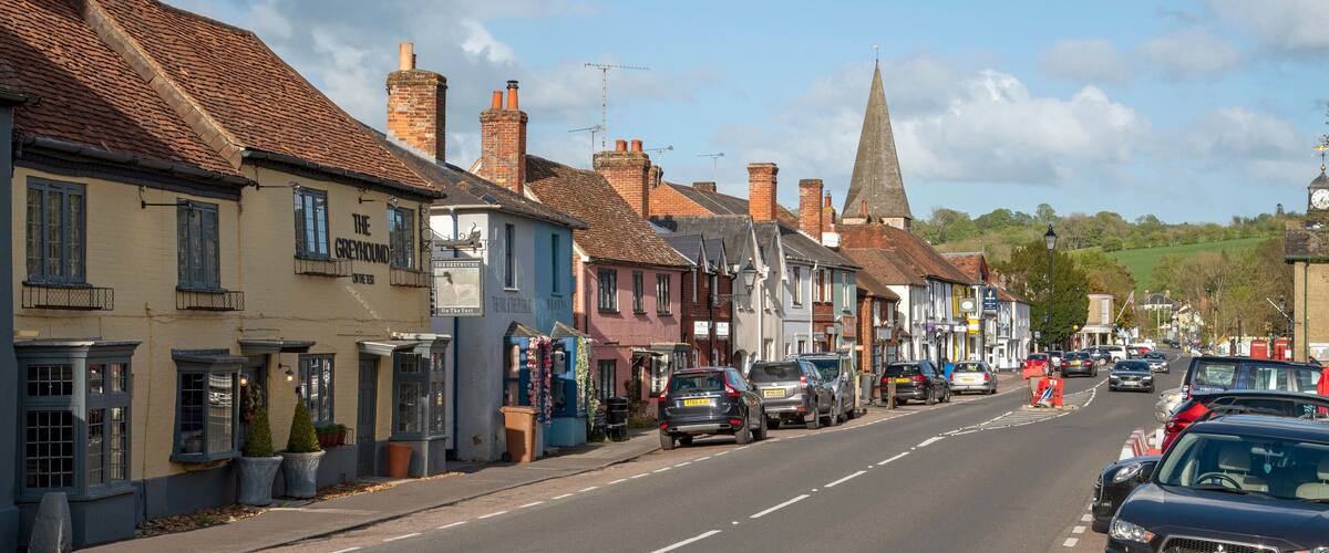A street lined with historic buildings, a church spire, and parked cars.