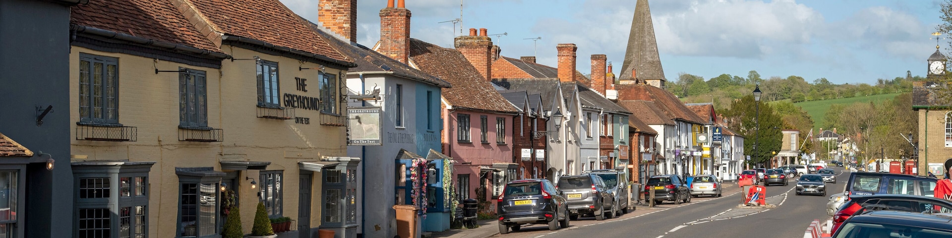 A street lined with historic buildings, a church spire, and parked cars.