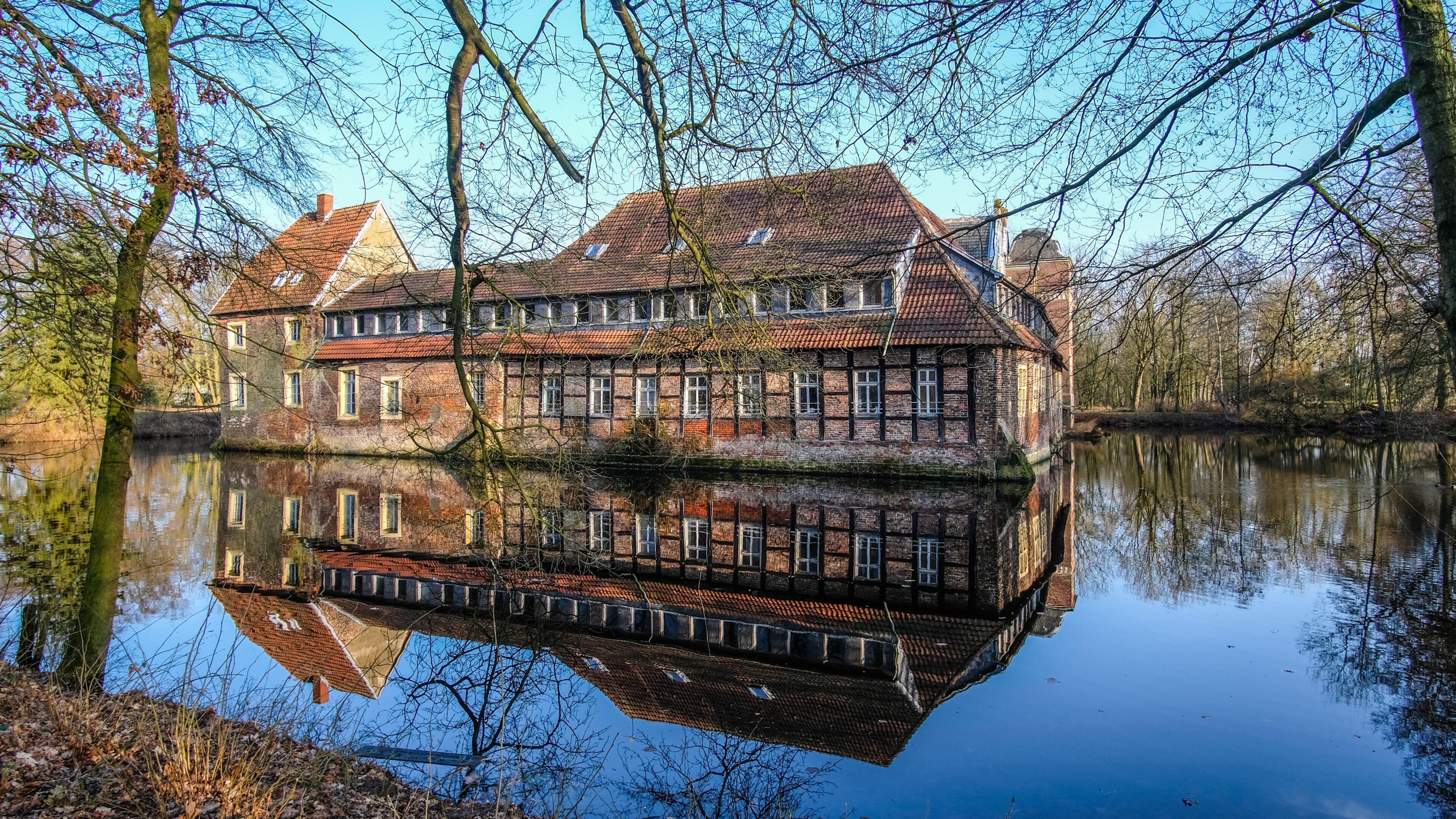 A historic building with a reflection in the water, surrounded by trees and a clear sky.