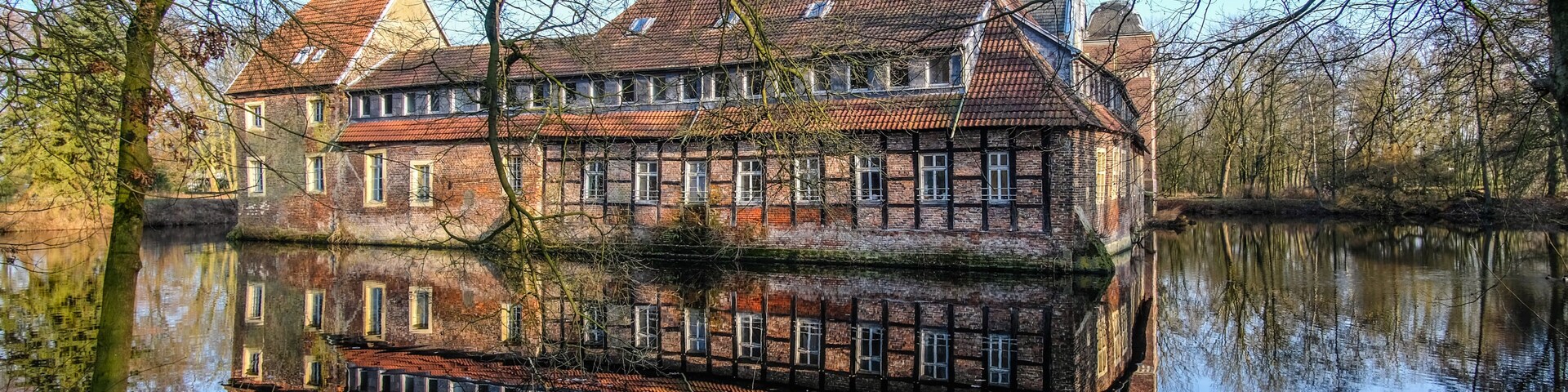 A historic building with a reflection in the water, surrounded by trees and a clear sky.