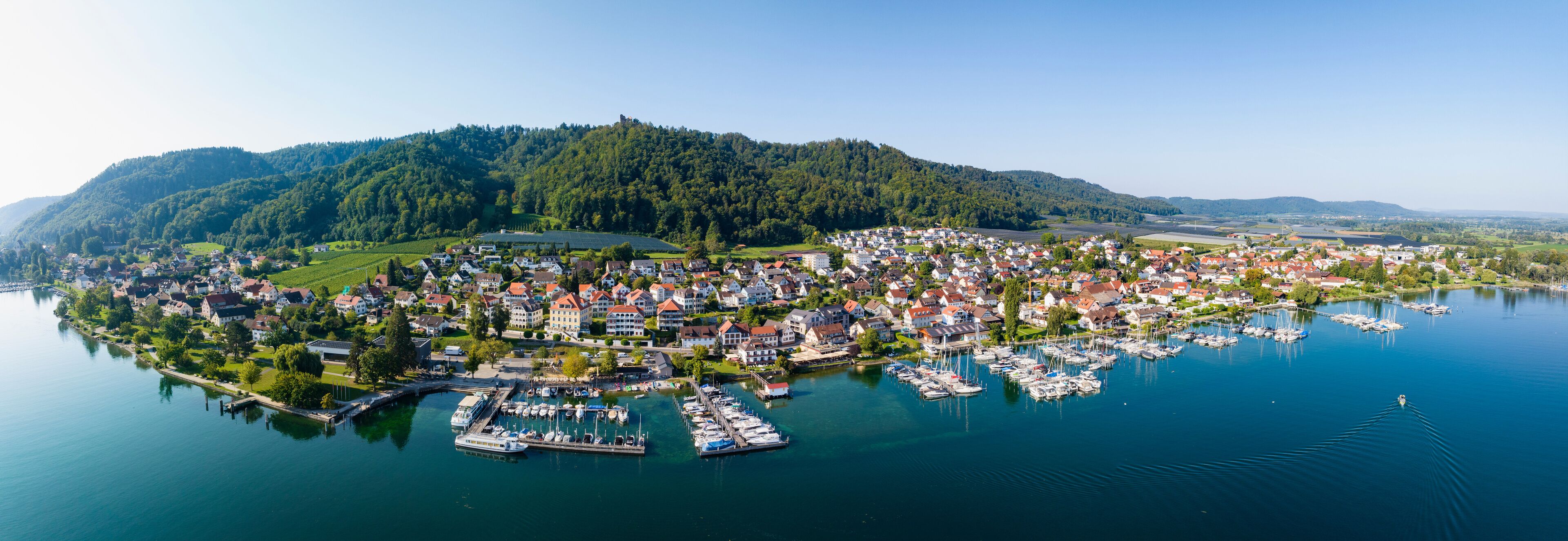A lakeside town with a marina, surrounded by hills and greenery.