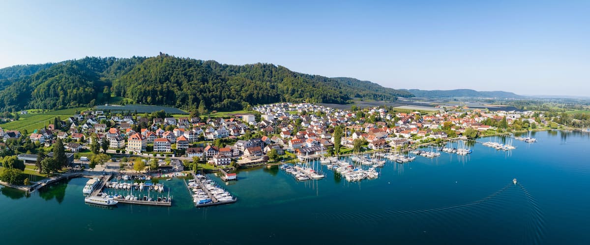 A lakeside town with a marina, surrounded by hills and greenery.