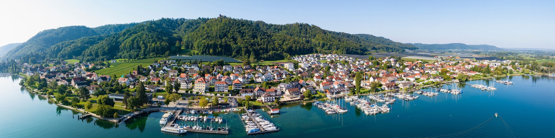 A lakeside town with a marina, surrounded by hills and greenery.