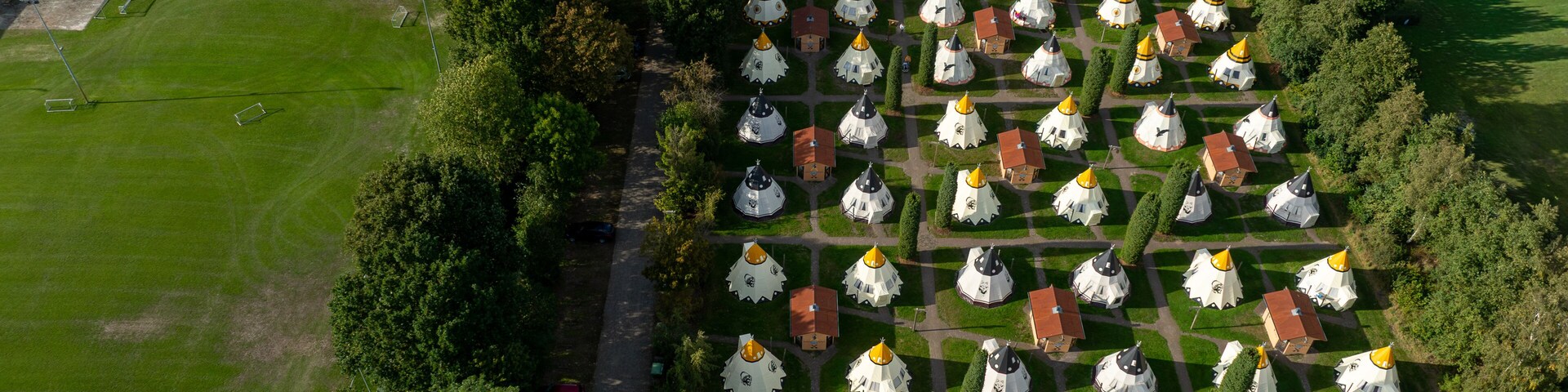 An aerial view of a park with a large green field, rows of white and yellow domed structures, and a sports field.