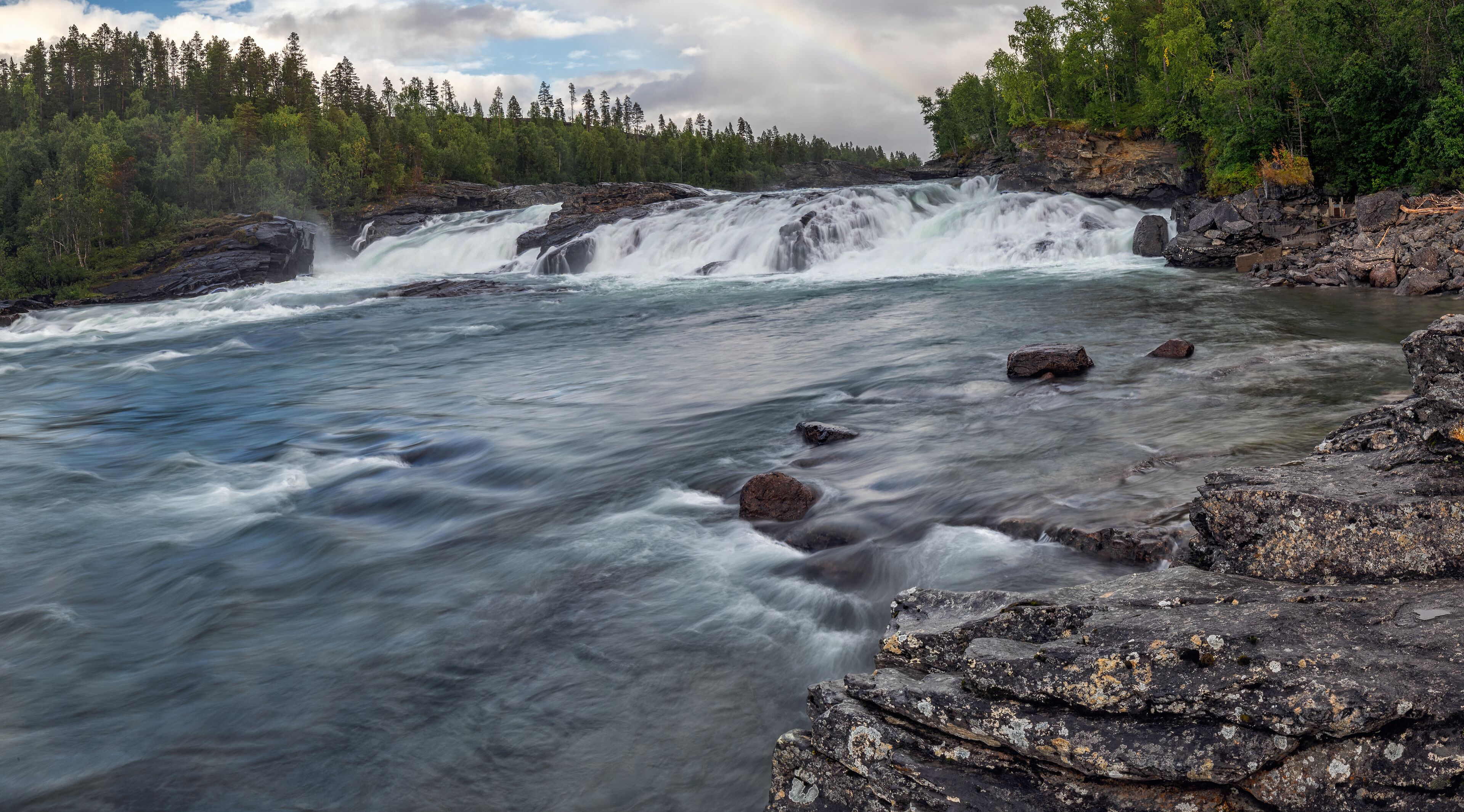 A river with a waterfall, surrounded by dense forest and rocky terrain.