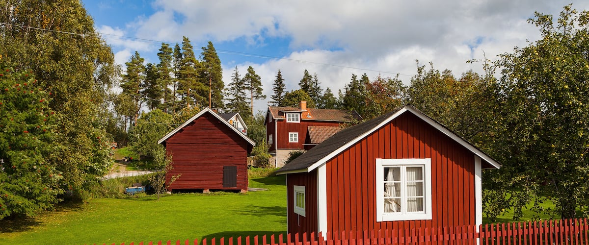 A red wooden house with a white window, surrounded by a red picket fence and a green lawn.