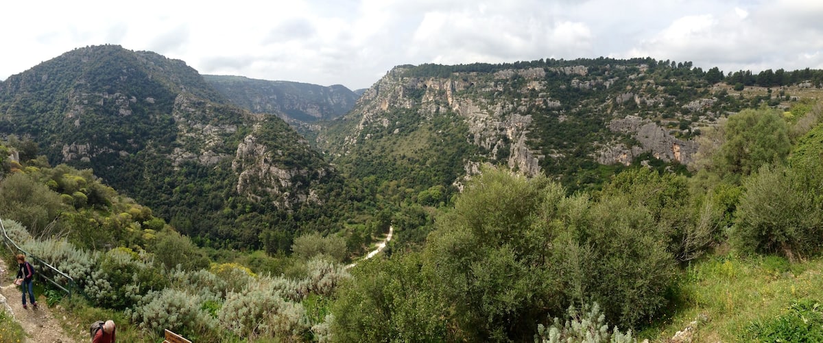 A mountainous landscape with a hiking trail, rocky cliffs, and dense greenery.