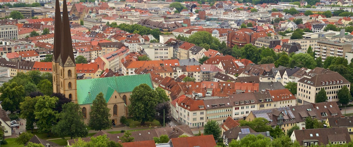 A cityscape with a prominent church with a tall spire and a green-roofed building.