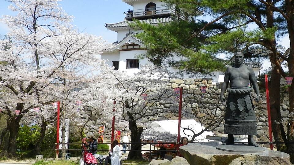 A traditional Japanese building with a pagoda, cherry blossom trees, and a statue.