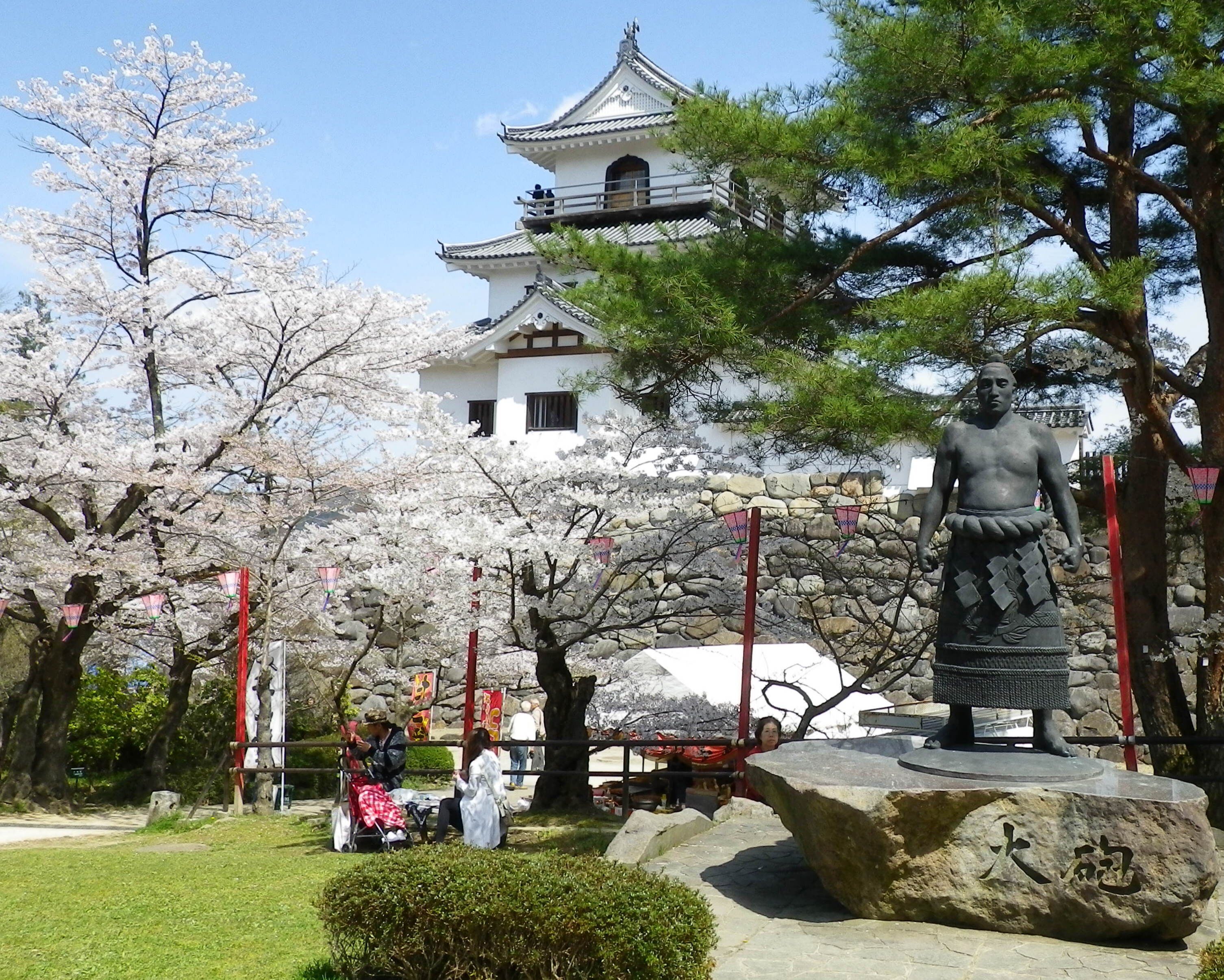 A traditional Japanese building with a pagoda, cherry blossom trees, and a statue.