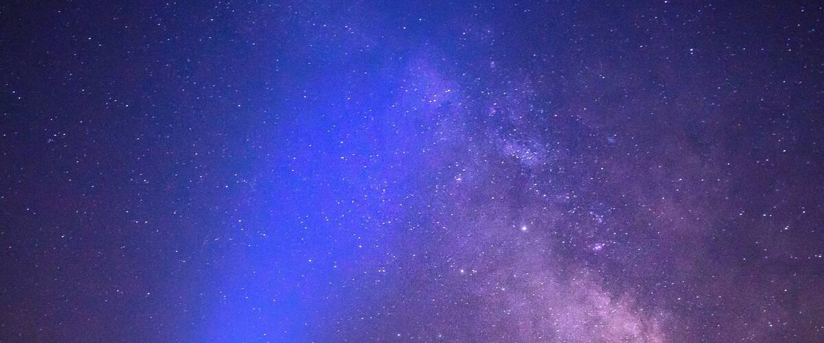 A person standing on a beach under a starry sky with a blue light beam.