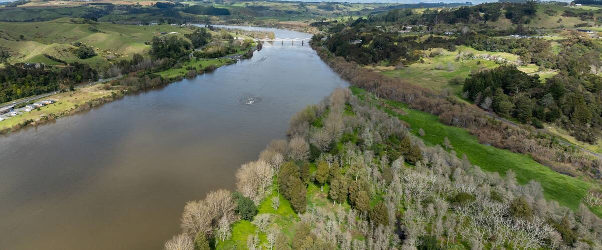 A river with a bridge, surrounded by green hills and trees.