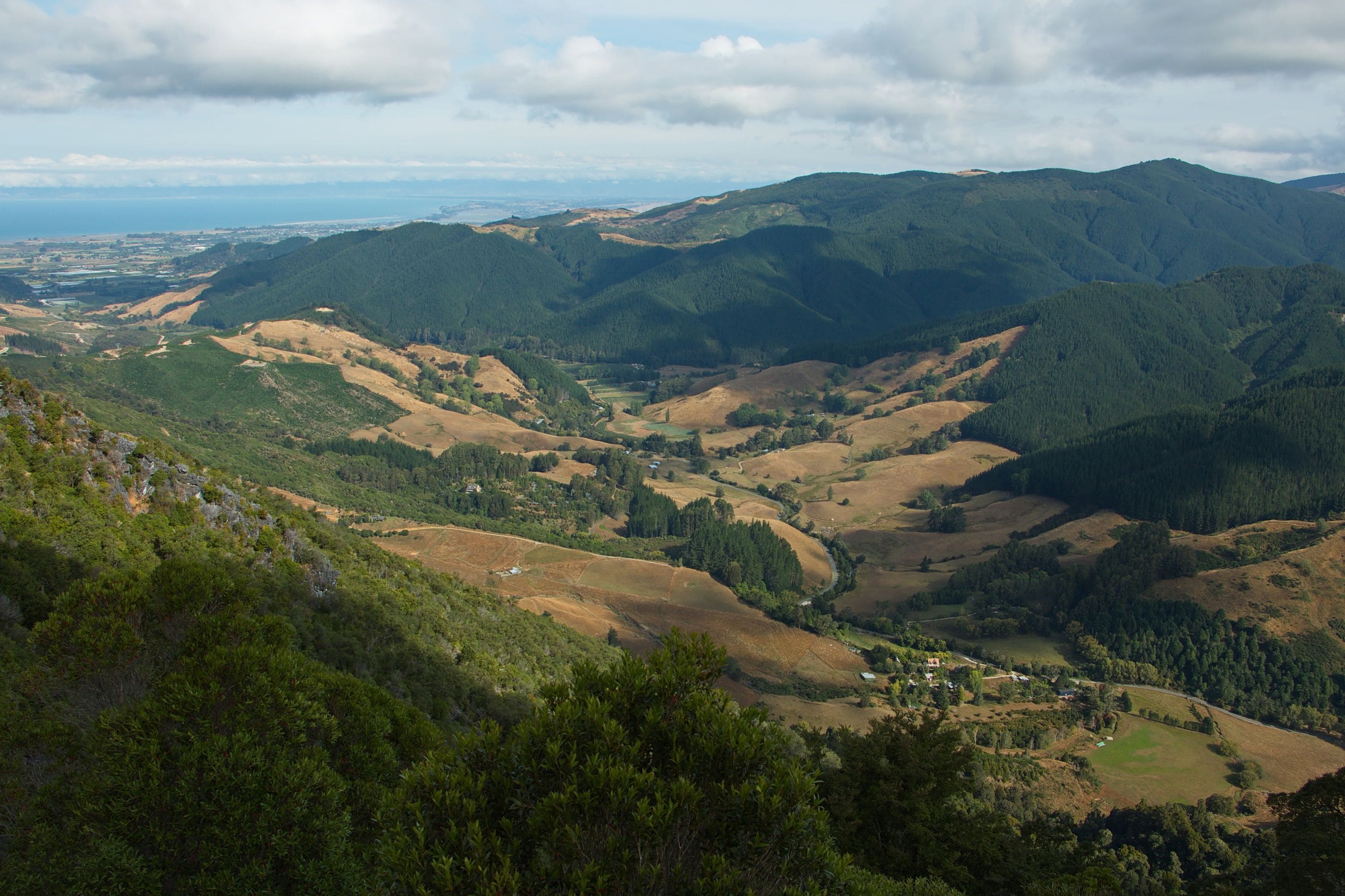A mountainous landscape with valleys, forests, and a distant view of a coastline.