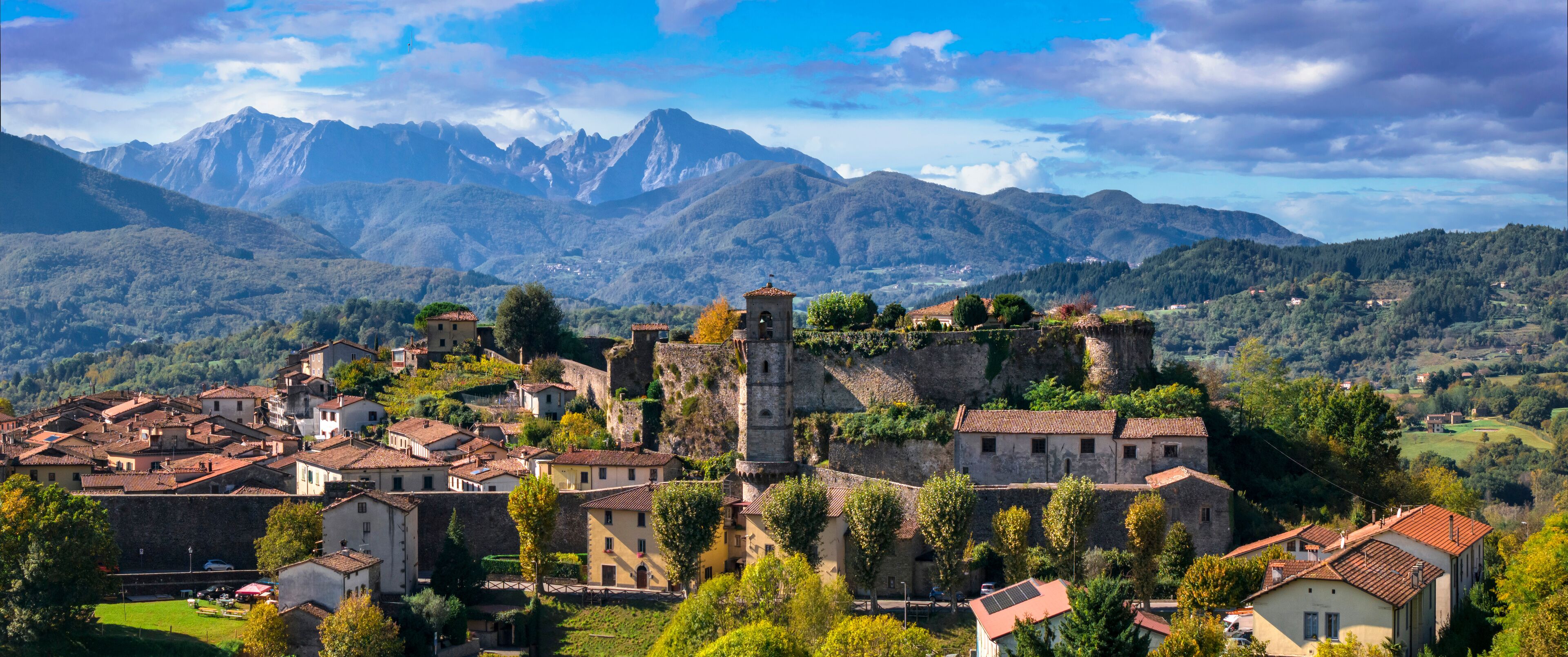 A historic town with medieval architecture, surrounded by mountains and lush greenery.