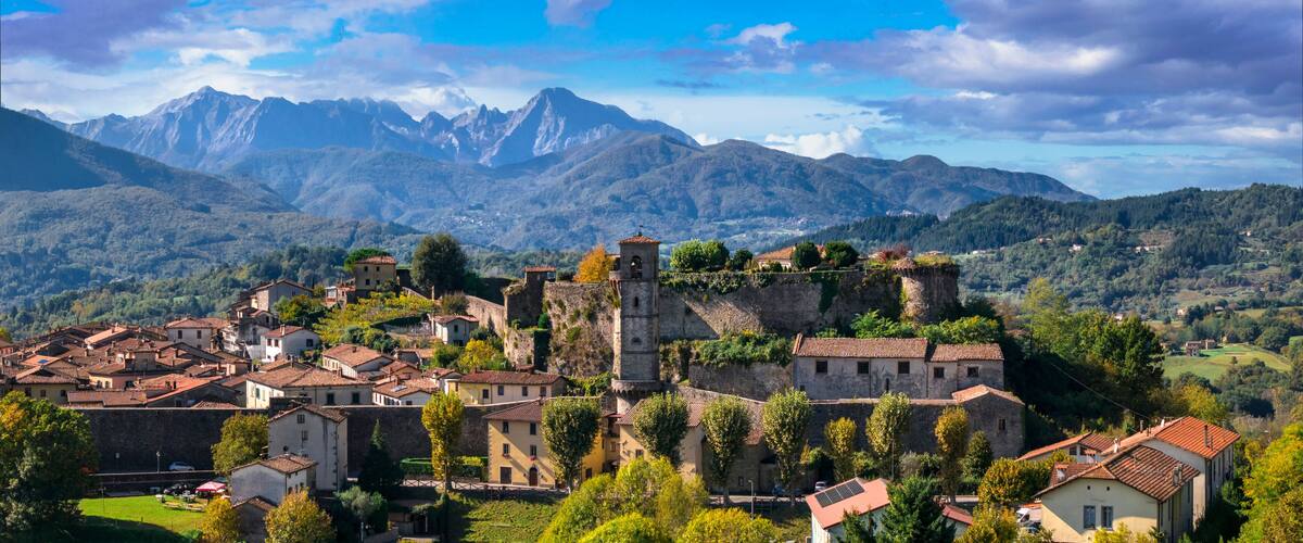 A historic town with medieval architecture, surrounded by mountains and lush greenery.