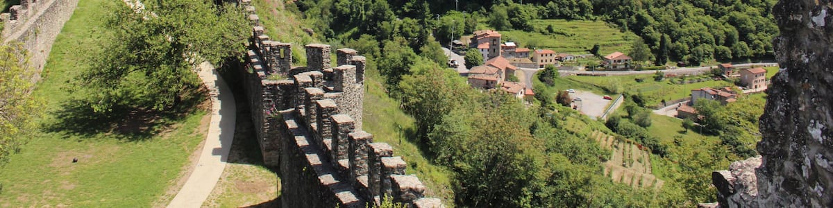 Eine historische Steinmauer mit Ruinen, ein Dorf und üppige, grüne Hügel.