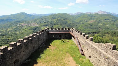 A historic stone fortress with a surrounding wall, set against a backdrop of lush green hills and distant mountains.