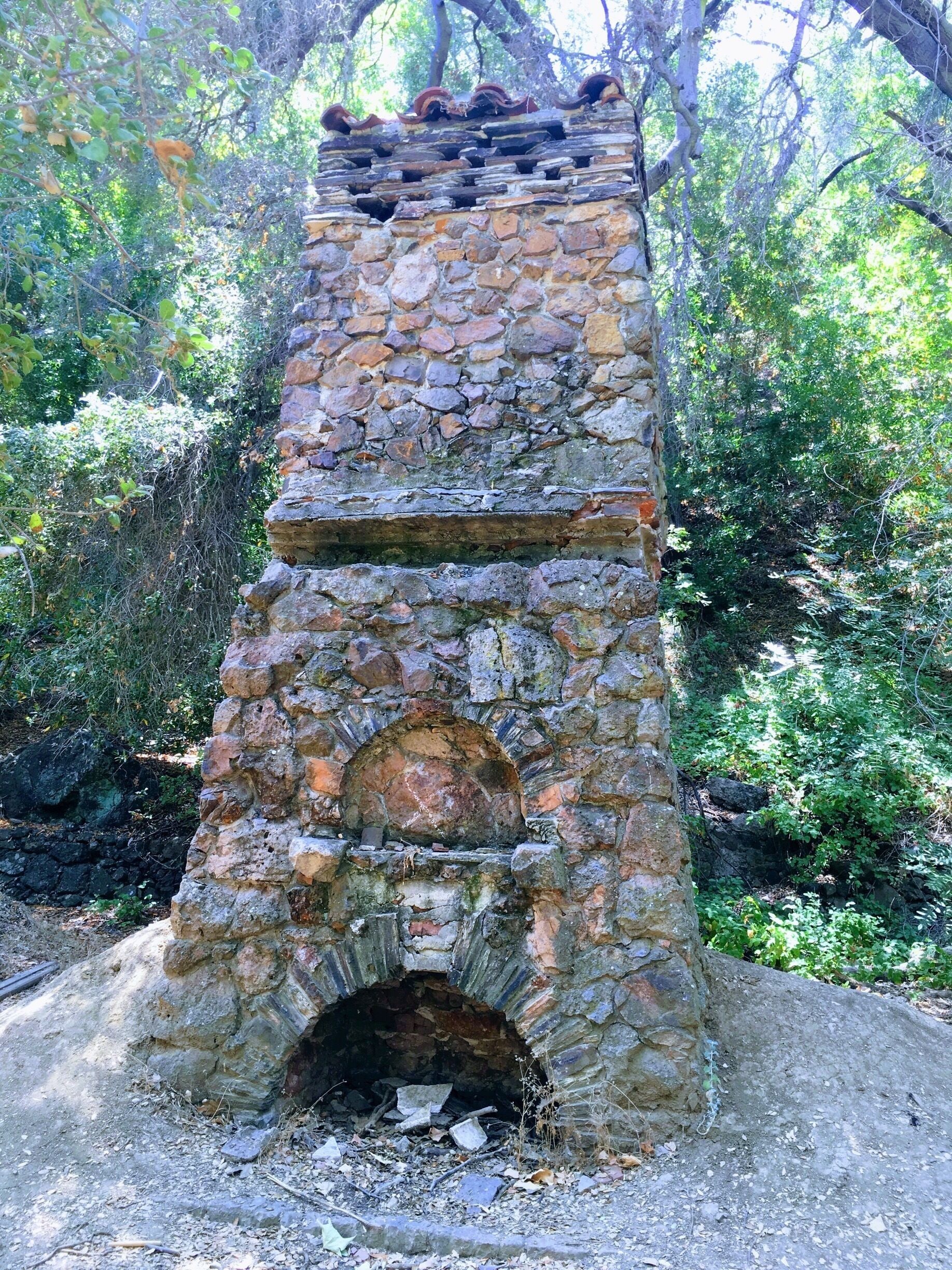 Una estructura de piedra con una abertura circular en la base, rodeada de vegetación.