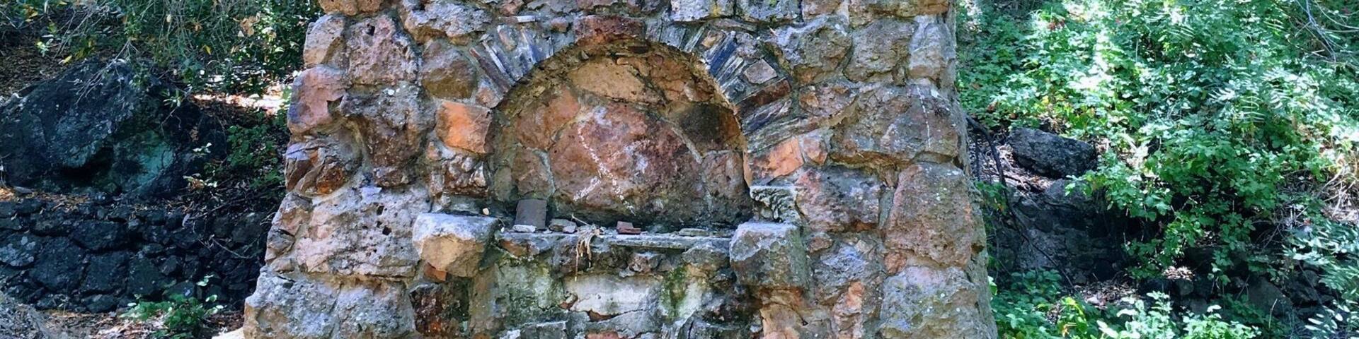 Una estructura de piedra con una abertura circular en la base, rodeada de vegetación.