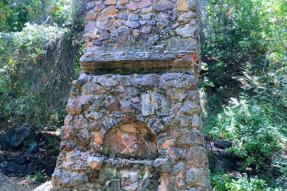 A stone structure with a circular opening at the base, surrounded by greenery.