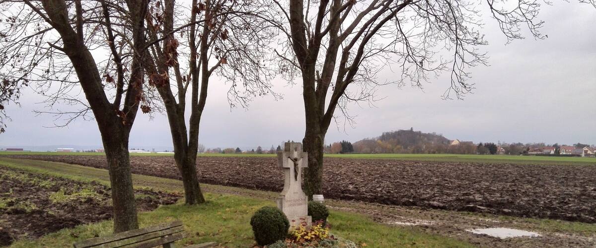 A rural landscape with a gravestone, a bench, and a plowed field.