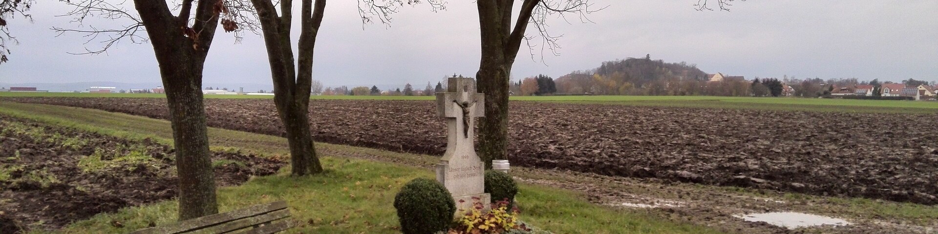 A rural landscape with a gravestone, a bench, and a plowed field.