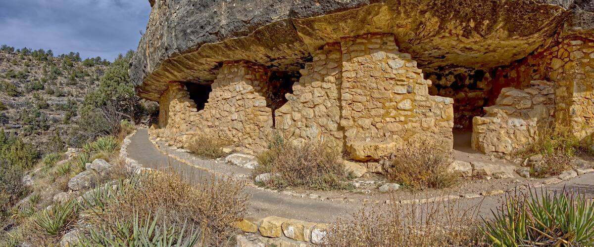A stone ruin with a cave-like structure, surrounded by dry vegetation and a winding path.
