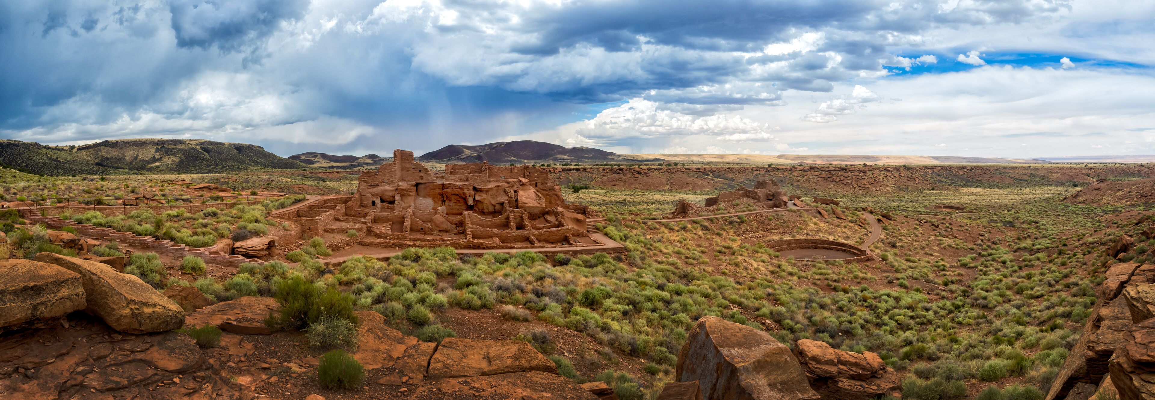 Ancient ruins in a desert landscape with distant mountains and a cloudy sky.