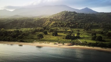 A river with a sandy beach, lush green hills, and a mountain in the background.
