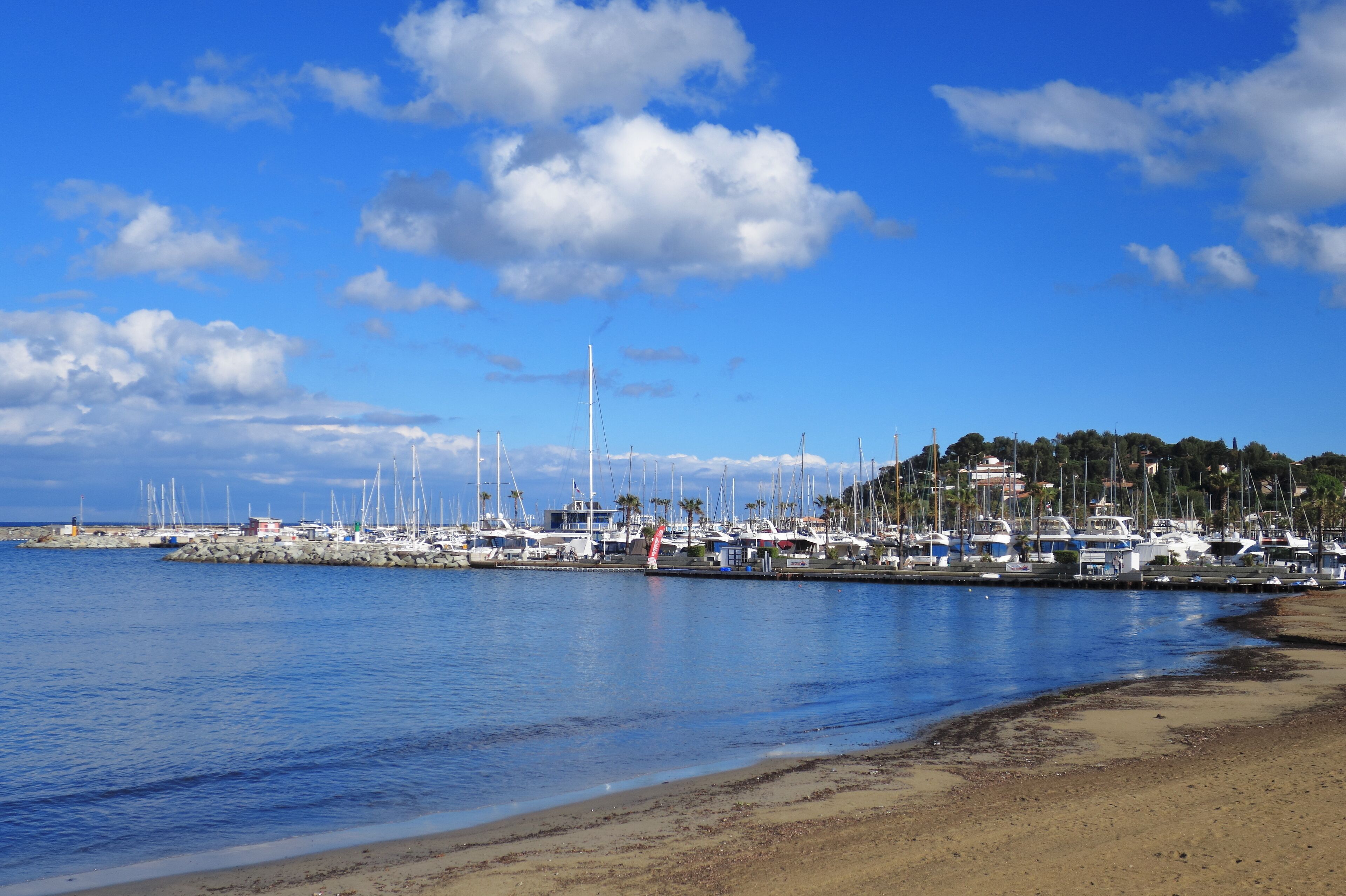 A marina with boats docked along a sandy beach under a clear blue sky.