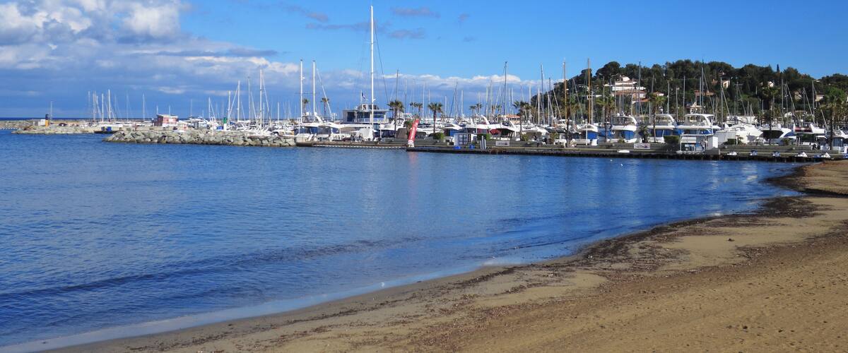 A marina with boats docked along a sandy beach under a clear blue sky.