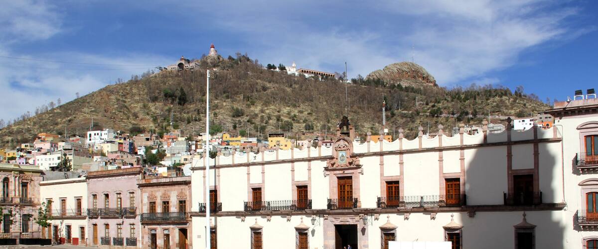 A town with historic buildings and a prominent hill with a church on top.