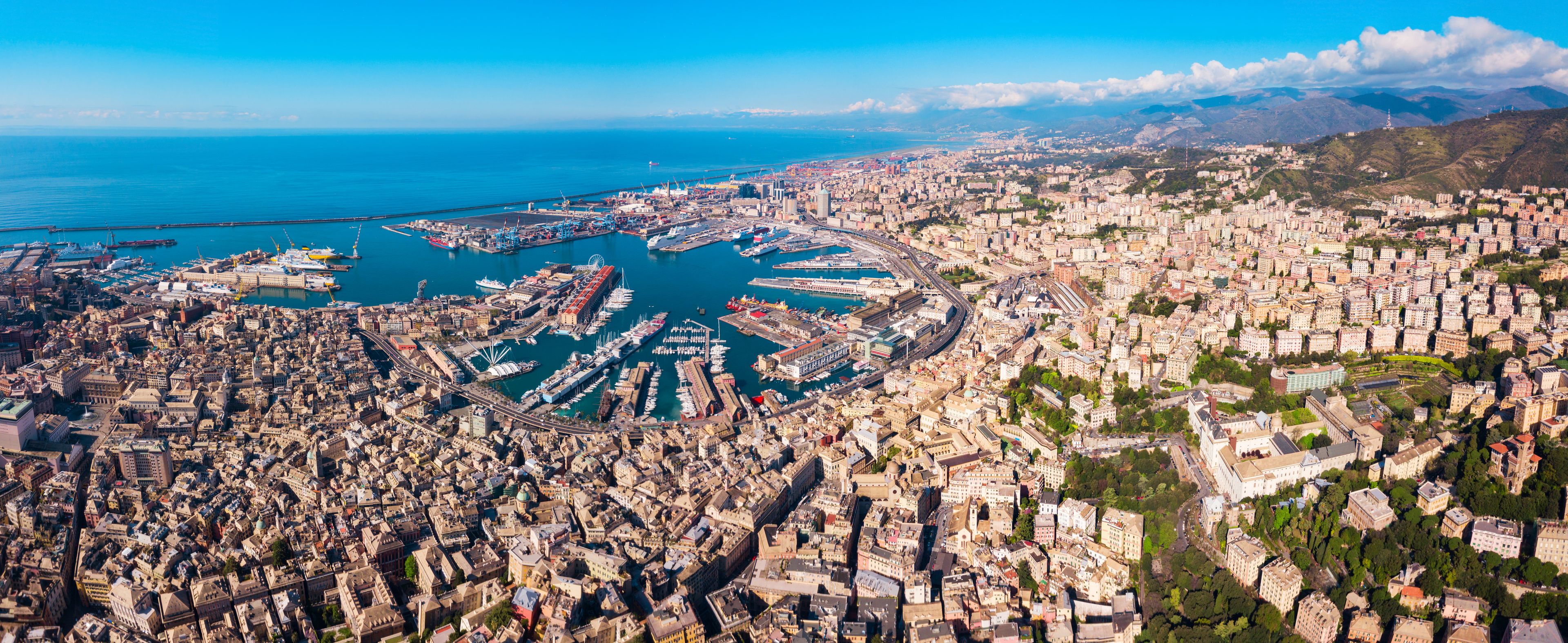 Una ciudad costera con una zona urbana densa, un puerto deportivo y montañas al fondo.