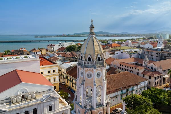 A coastal cityscape with a prominent church tower, a river, and distant mountains.