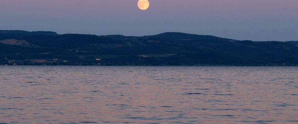 A full moon over a calm lake with hills in the background.