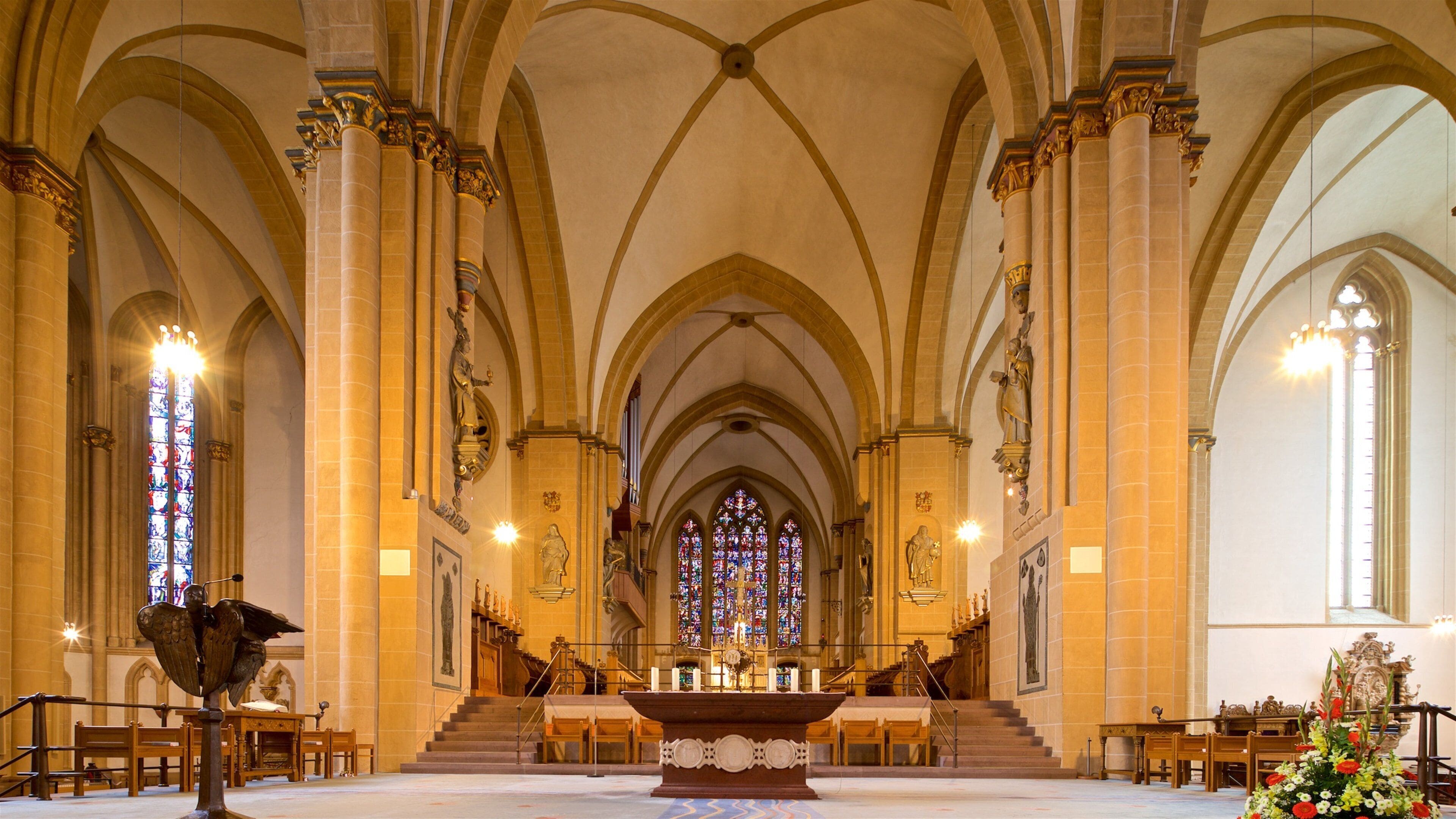Interior de una catedral con altas bóvedas, vidrieras y un altar central.