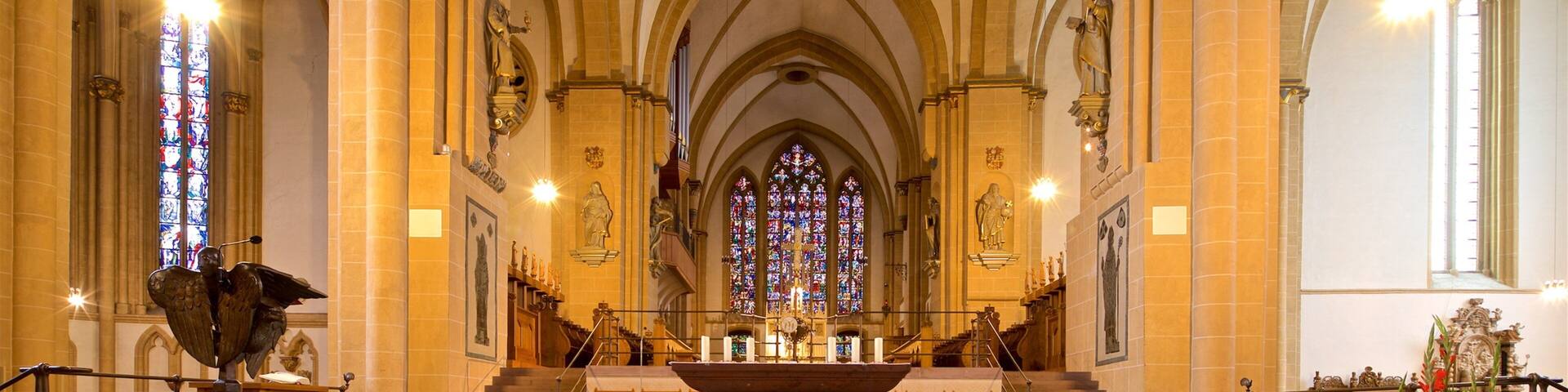A cathedral interior with high vaulted ceilings, stained glass windows, and a central altar.