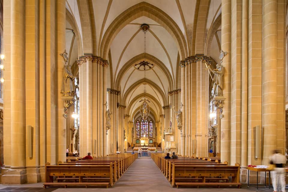 Een kathedraalinterieur met hoge gewelfde plafonds, grote glas-in-loodramen en rijen houten banken.