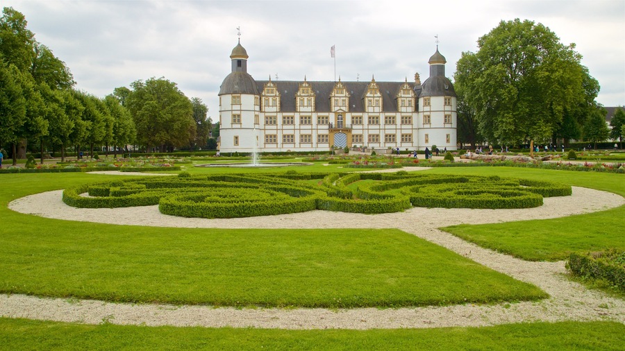 Un edificio grande y ornamentado con múltiples torres y un jardín cuidado con setos geométricos.