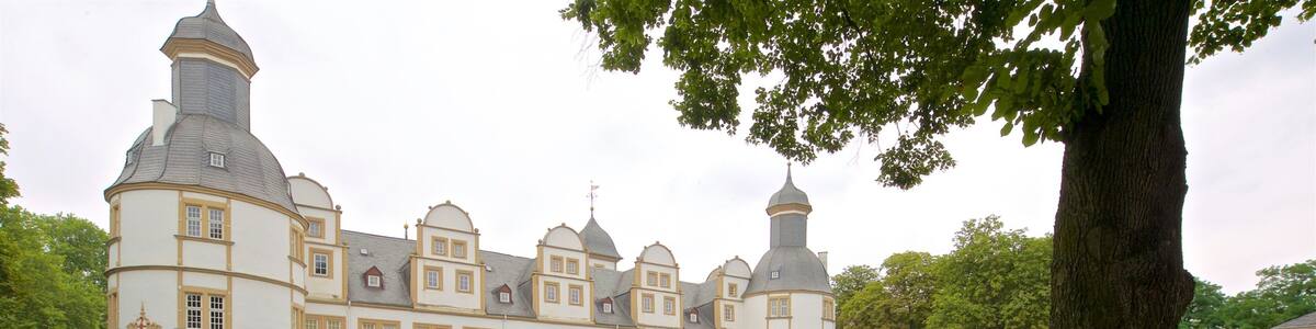 Ein großes, weißes Gebäude mit mehreren Türmen und einem gepflegten Garten mit roten und weißen Blumen.