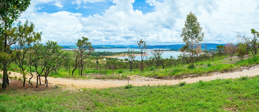 Beautiful panoramic landscape of the green vegetation, dirt road, hill, and a lake on the background. Landscape of Capitólio MG Brazil, Lago de Furnas lake on background.