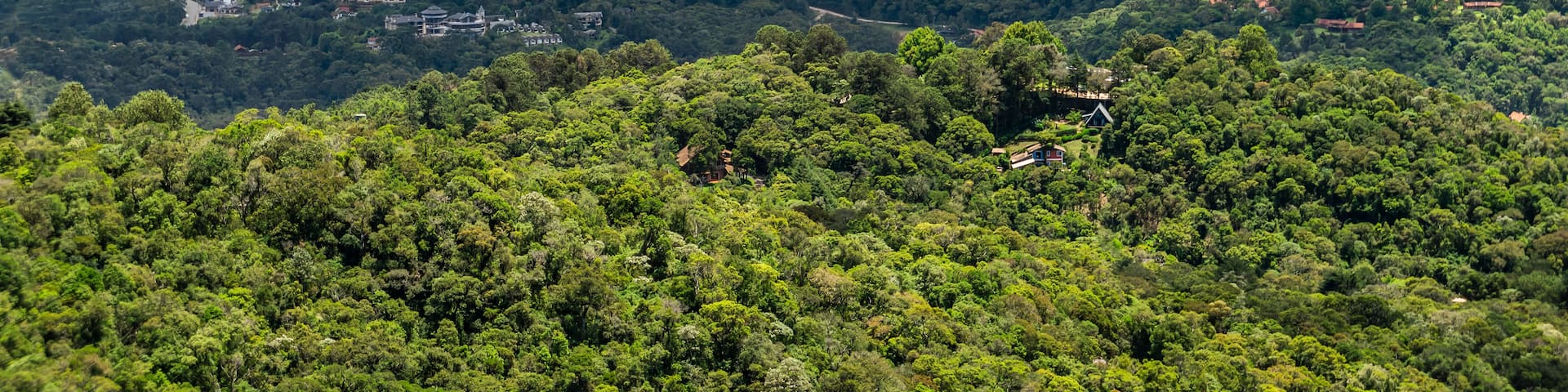 A mountainous landscape with dense forests, scattered buildings, and winding roads.